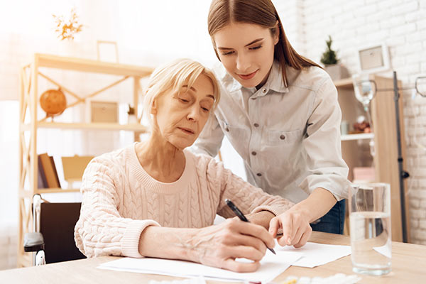 Pflegekraft hilft einer älteren Frau beim Schreiben